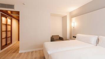 Una habitación de hotel con una cama, una silla, una lámpara de pared y una puerta de madera.