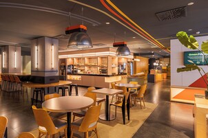 Un restaurante moderno con mesas y sillas redondas, una zona de bar y una pantalla digital que muestra 'Green Friday'.