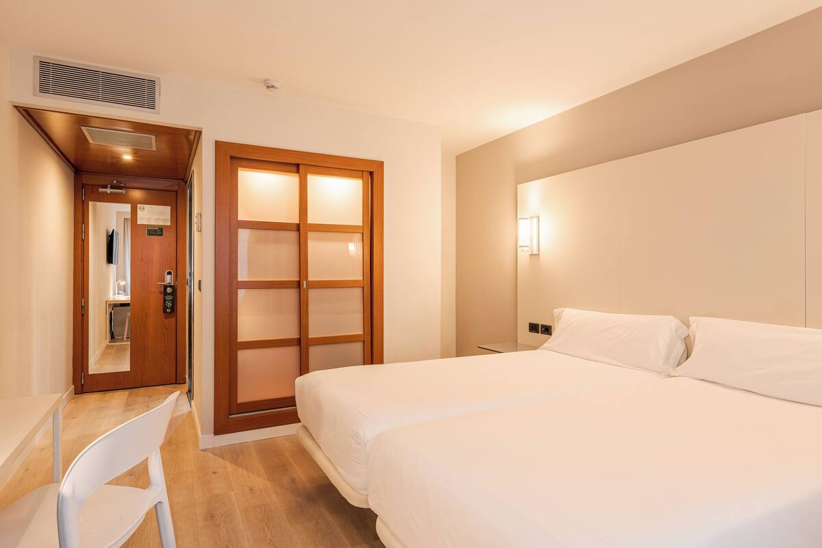 Una habitación de hotel con cama, escritorio, silla y puerta corrediza.