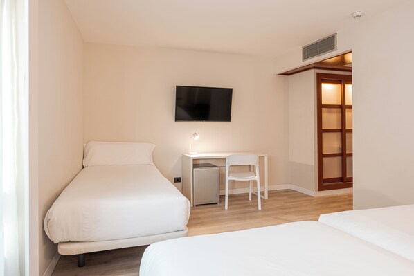 A bedroom with two beds, a desk with a chair, a TV, and a small heater. - B&B Hotel Castellon (Castelló de la Plana)
