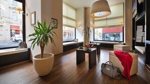A modern hotel room with a large window, wooden flooring, a potted plant, a black table, a white sofa, and a red throw blanket. - Hotel Suite Home Prague (Prague)