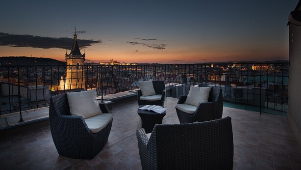 A balcony with wicker furniture and a view of a cityscape at dusk. - Hotel Suite Home Prague (Prague)