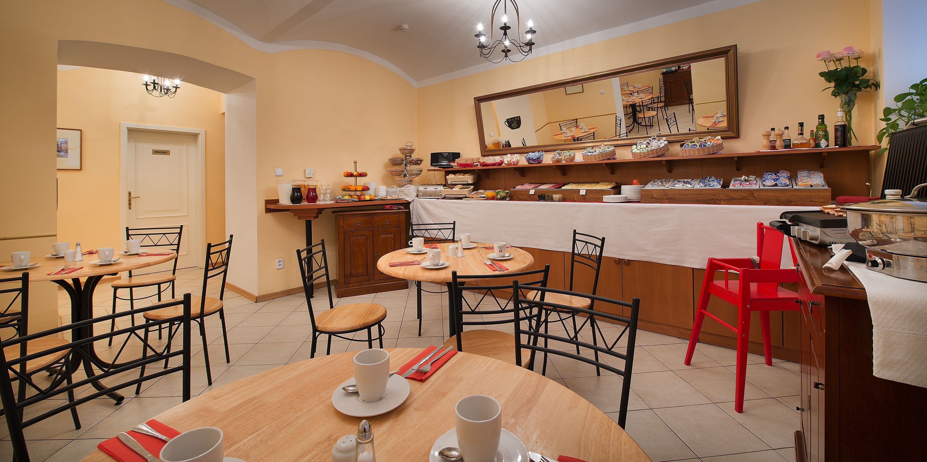 A dining area with wooden tables and chairs, a buffet counter with various food items, and a large mirror on the wall.