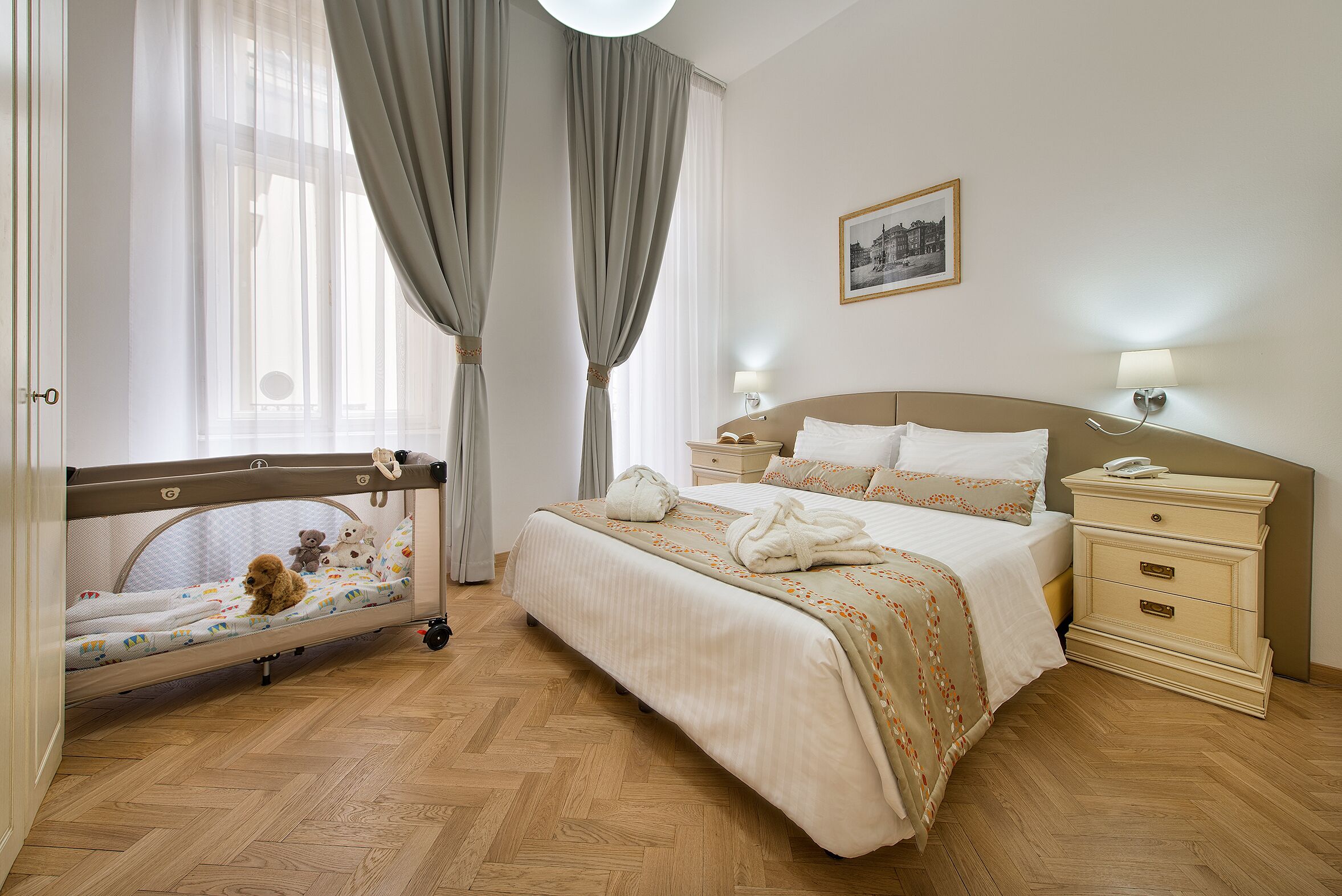 Habitación de hotel con cama, mesitas de noche, cortinas y un osito de peluche sobre la cama.