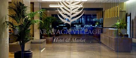 A modern hotel lobby with a large leaf-shaped sign, potted plants, and a reception desk.