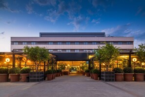 A modern hotel with a flat roof, large windows, and a covered entrance area with potted plants. - Hotel Aravaca Village (Madrid)