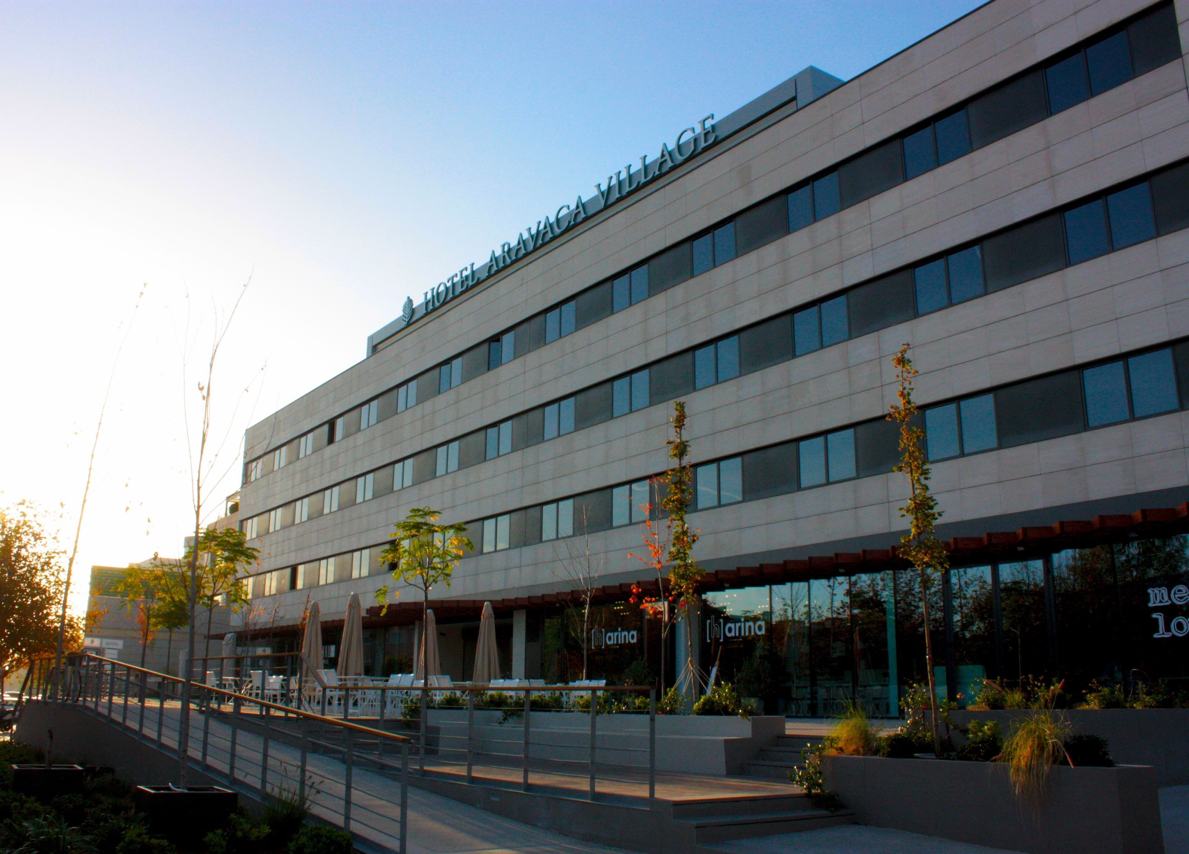 A modern hotel with a flat roof, multiple floors, and a covered outdoor seating area with umbrellas.
