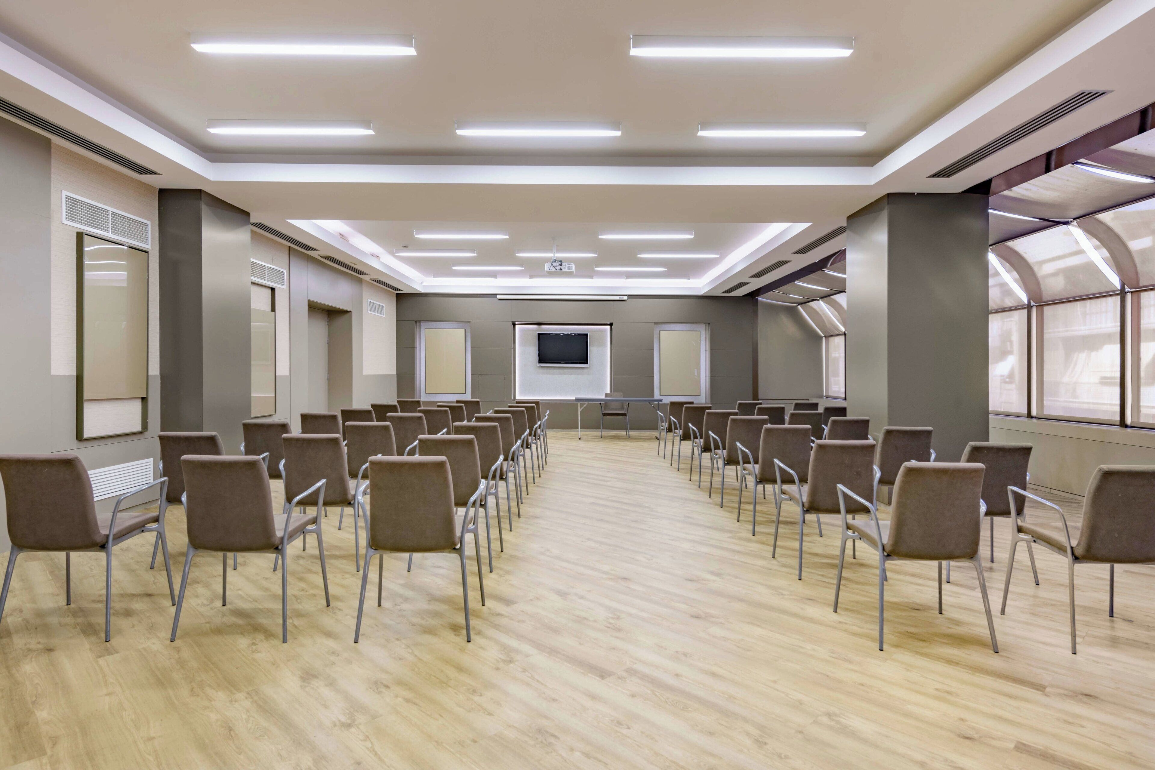 Un salón de conferencias con filas de sillas, una pantalla grande y un proyector.