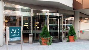 A hotel entrance with a revolving door, a sign for AC Hotels Marriott, and two potted plants. - AC Hotel Genova by Marriott (Genoa)