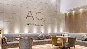 A modern hotel lobby with a sofa, chairs, and a round table. - AC Hotel Genova by Marriott (Genoa)