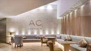 A modern hotel lobby with a sofa, chairs, and a table. - AC Hotel Genova by Marriott (Genoa)