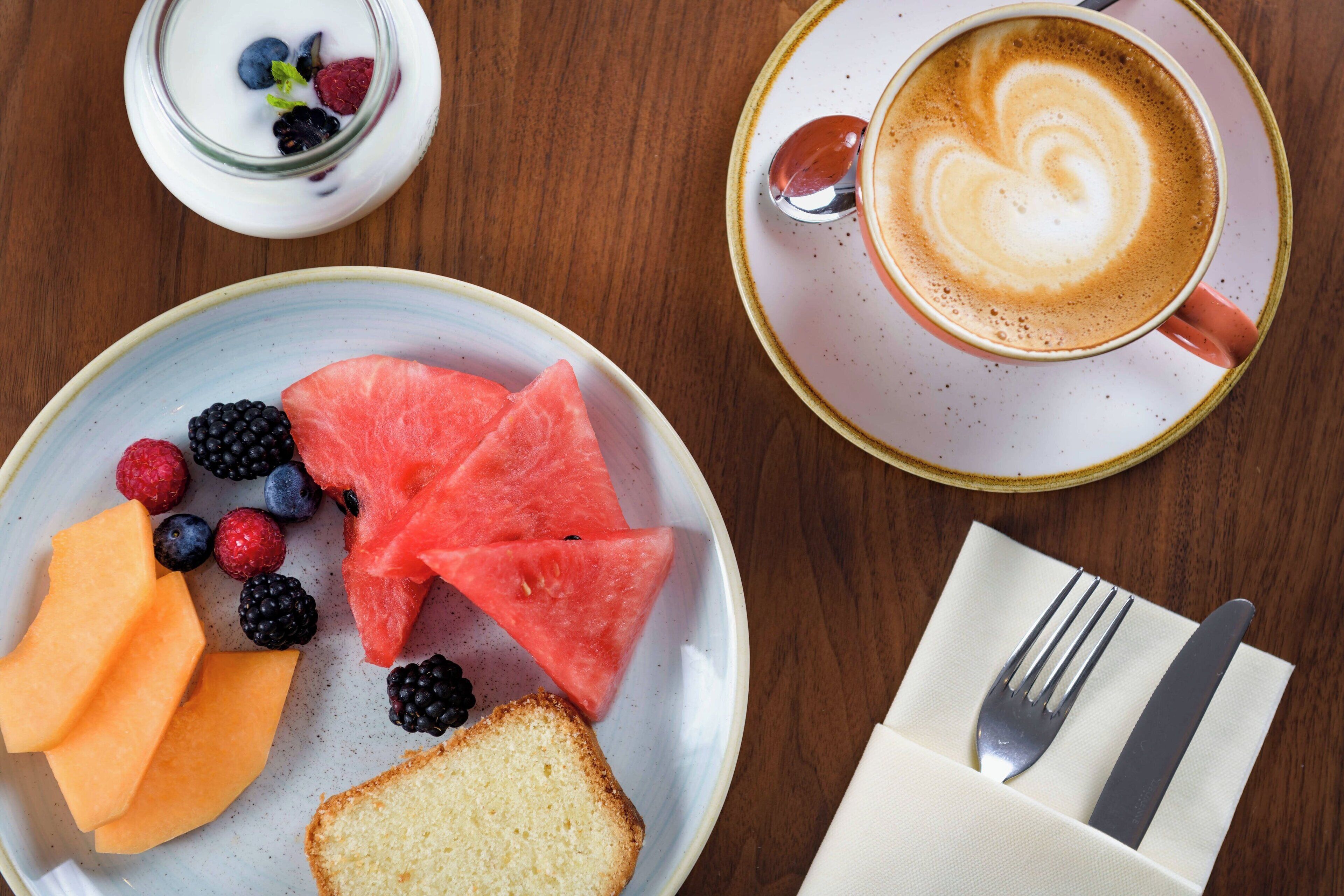 A breakfast setting with a plate of fruit, a cup of coffee, and a small bowl of yogurt.