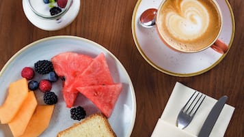 A breakfast setting with a plate of fruit, a cup of coffee, and a small bowl of yogurt.