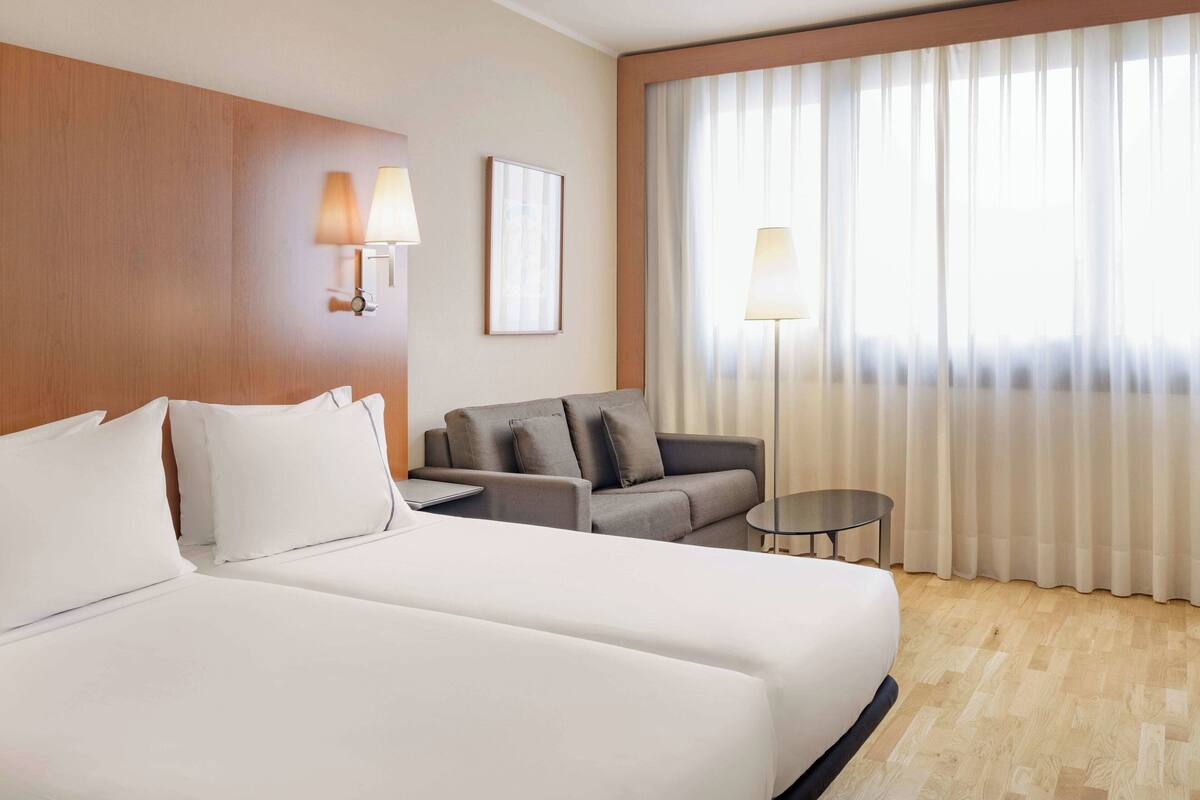 A hotel room with a large bed, a sofa, a small table, and a lamp.
