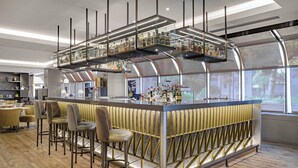 A modern bar area with a central counter, bar stools, and a display of liquor bottles. - AC Hotel Genova by Marriott (Genoa)