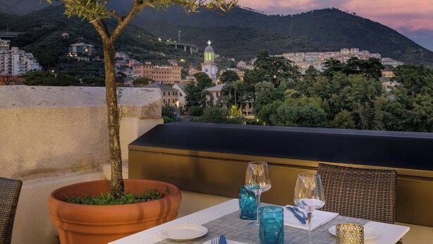 A terrace with a table set for two, overlooking a cityscape with buildings and a hill. - AC Hotel Genova by Marriott (Genoa)