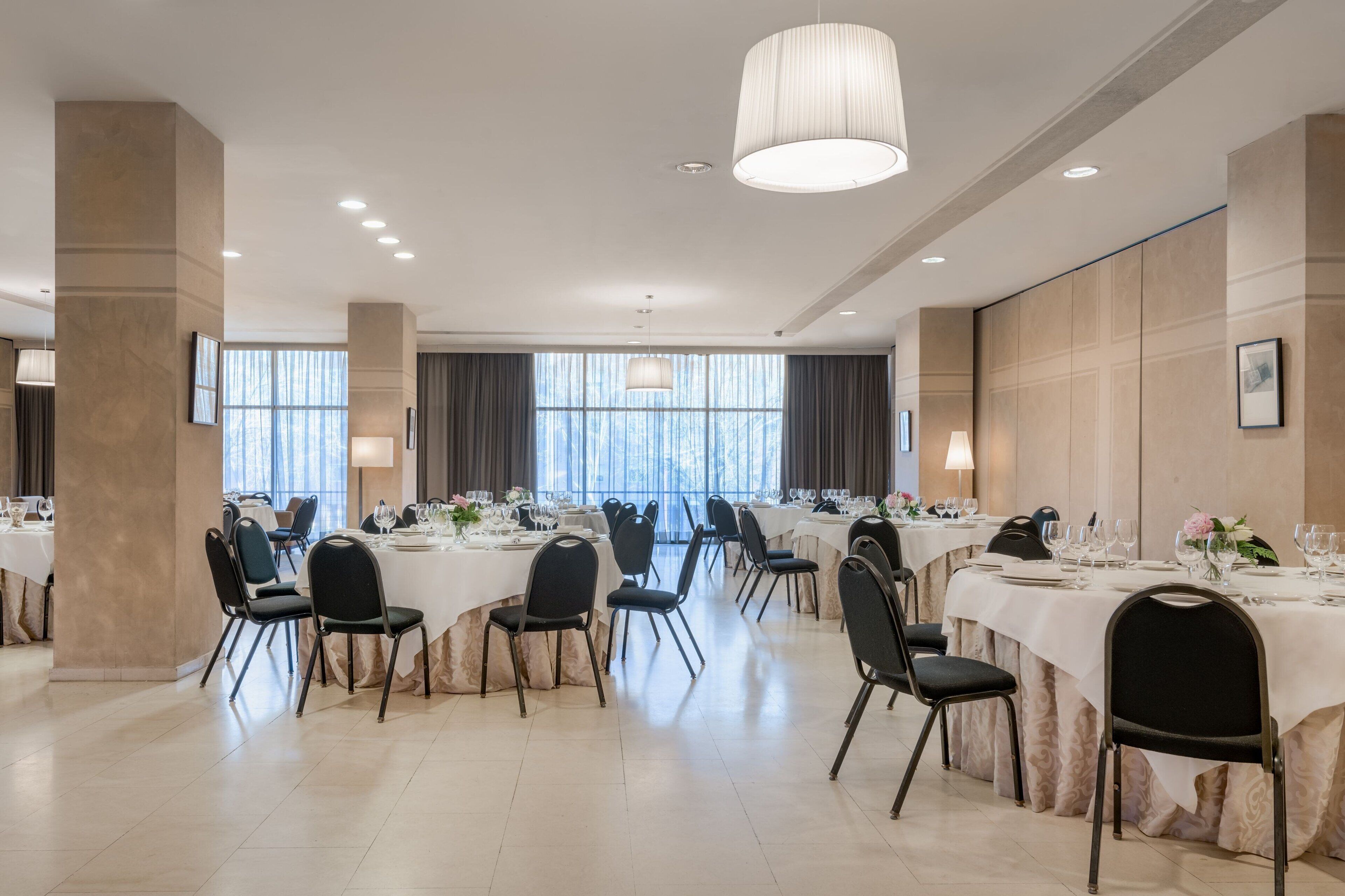 A spacious dining area with multiple round tables, black chairs, and a large chandelier.