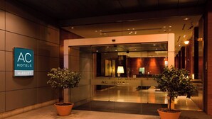 Exterior do AC Hotels Marriott com entrada moderna, duas plantas em vasos e fachada de vidro.