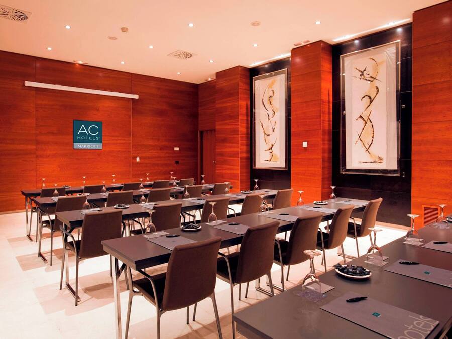 Une salle de conférence avec de longues tables et des chaises, une enseigne indiquant « AC Hotels Marriott », et deux grandes œuvres d’art encadrées accrochées aux murs.