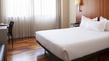 A hotel room with a large bed, a desk, a chair, and a nightstand with a lamp.