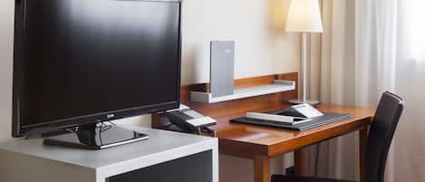 Habitación de hotel con escritorio, televisor de pantalla plana, lámpara, silla y un mueble bajo.