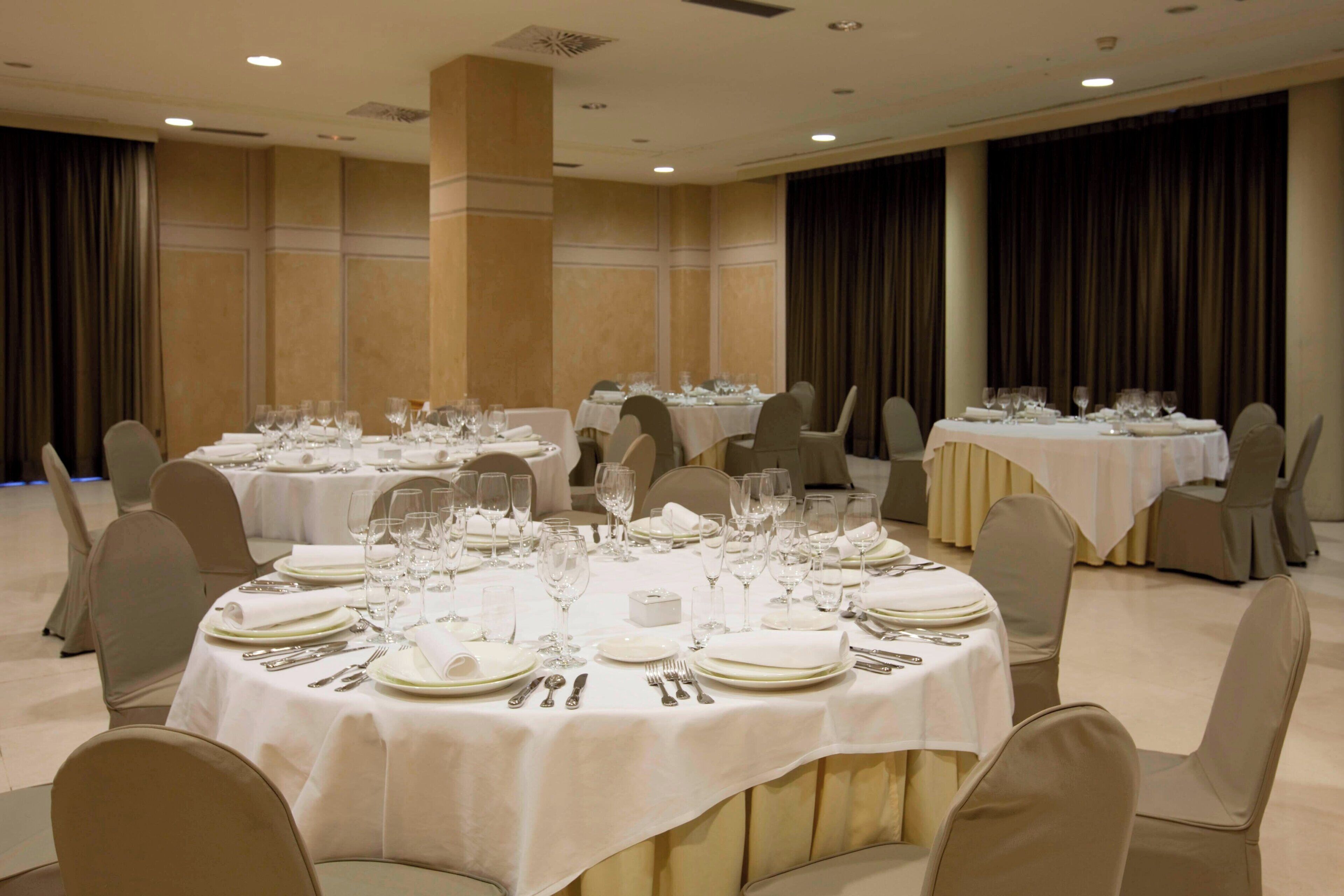 A banquet hall with round tables set for dining, each with white tablecloths and silverware.