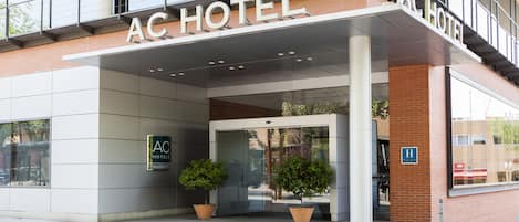 A hotel entrance with a modern design, featuring a glass door and a sign that reads "AC HOTEL."