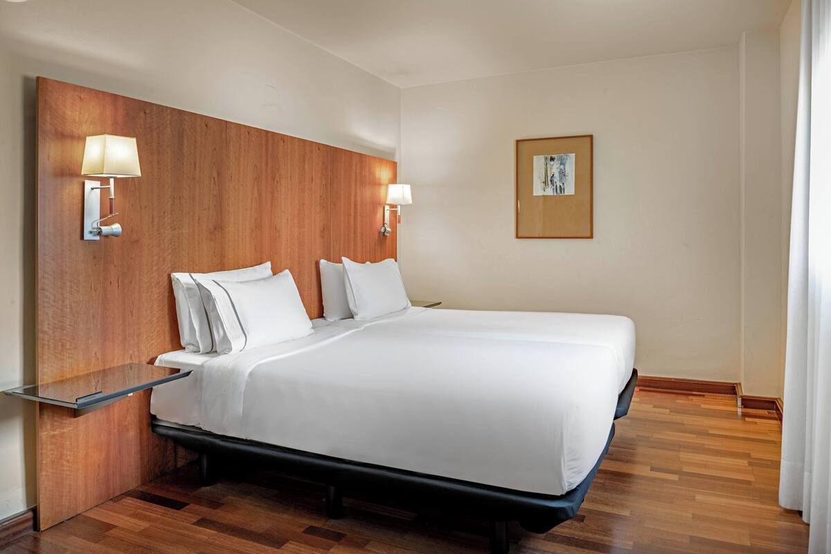 A hotel room with a large bed, wooden headboard, bedside lamps, and a framed picture on the wall.