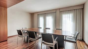 A conference room with a long table and six chairs, large windows with curtains, and wooden flooring.