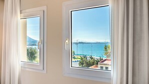 Two windows with white frames and curtains, each offering a view of a body of water, a distant mountain, and a cityscape. - AC Hotel La Línea by Marriott (La Línea de la Concepción)