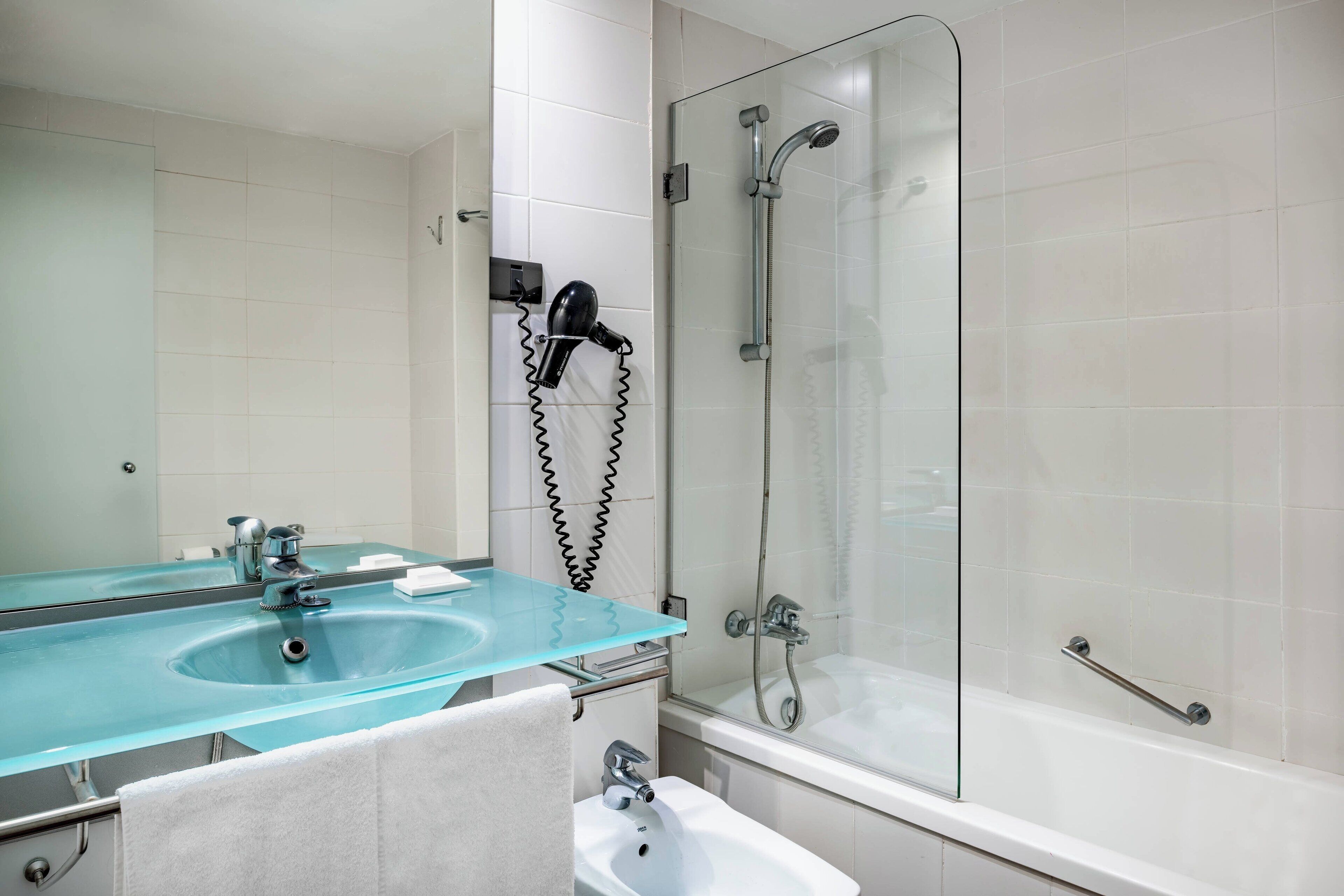 A bathroom with a glass sink, a mirror, a shower, and a bathtub.