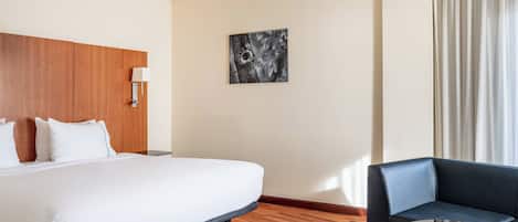 A hotel room with a large bed, a dark blue sofa, a round table, and a painting on the wall.