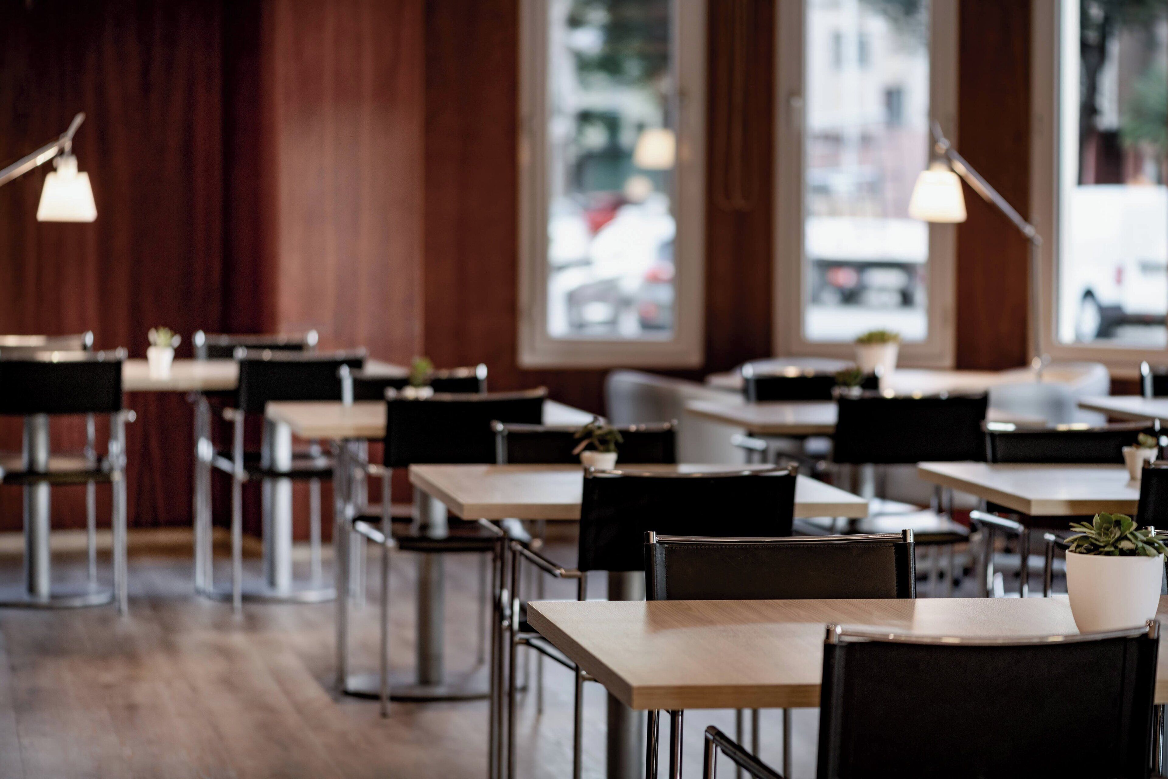 L’intérieur d’un restaurant avec des tables et des chaises en bois, des luminaires suspendus et des plantes en pot.