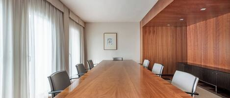 A conference room with a long wooden table, black chairs, and a wooden panel wall.