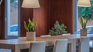 A modern dining area with a wooden table and white chairs, two potted plants, and pendant lighting. - AC Hotel La Línea by Marriott (La Línea de la Concepción)