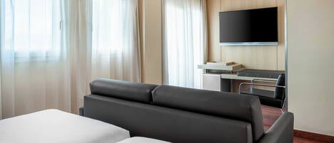 Habitación de hotel con dos camas, un escritorio, una silla, un televisor de pantalla plana y ventanas grandes con cortinas.