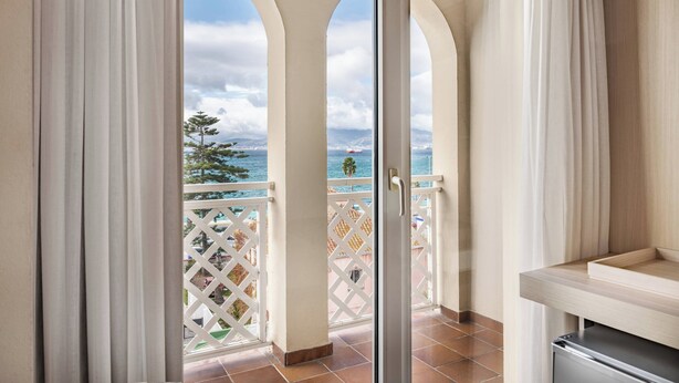 A balcony with a view of the sea and a ship, featuring a white lattice railing and a sliding glass door. - AC Hotel La Línea by Marriott (La Línea de la Concepción)