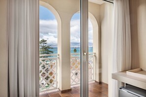 Un balcón con vista al mar y un barco, que cuenta con una barandilla blanca de celosía y una puerta corrediza de vidrio.