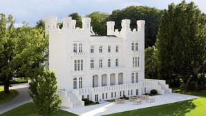 A large, white, castle-like building with multiple towers and arched windows, surrounded by lush greenery. - Grand Hotel Heiligendamm (Bad Doberan)