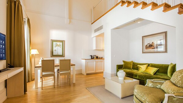 Una sala de estar moderna con un sofá verde, una mesa de centro y un comedor con sillas, con una cocina al fondo.