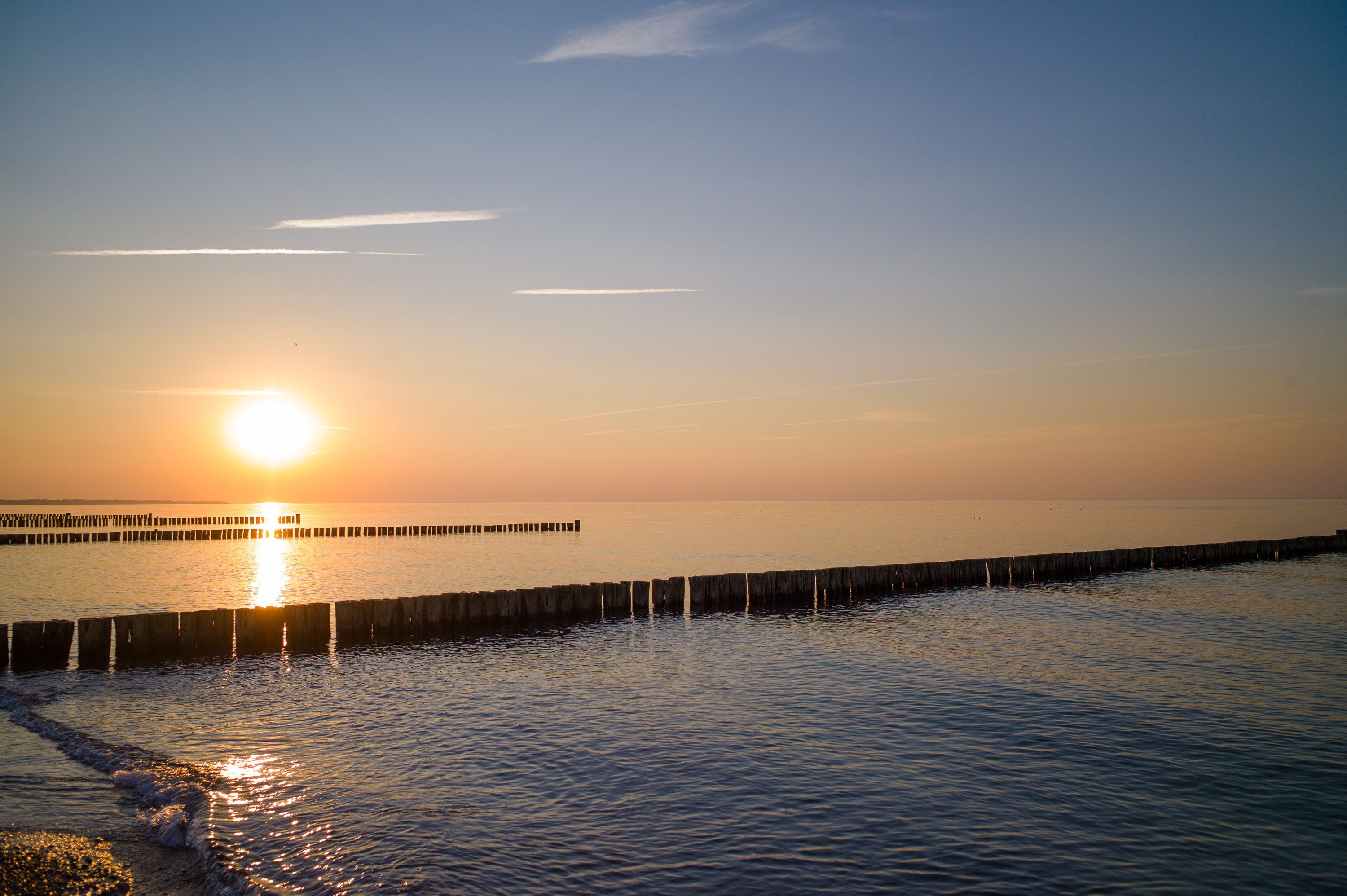 A sunset over a calm sea with a wooden pier extending into the water.