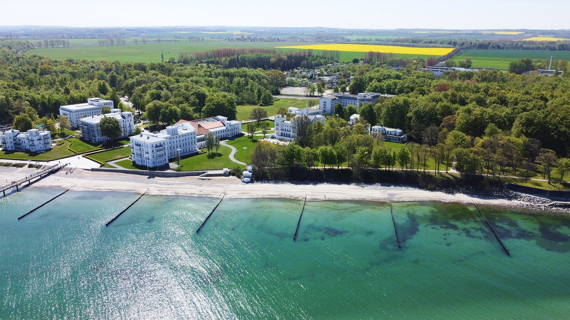 Vue aérienne d’un hôtel situé sur la côte, composé de plusieurs bâtiments, avec une jetée et une plage.