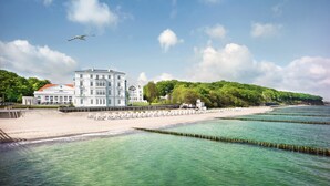A coastal building with a white facade and red roof, situated by a sandy beach and clear blue waters. - Grand Hotel Heiligendamm (Bad Doberan)