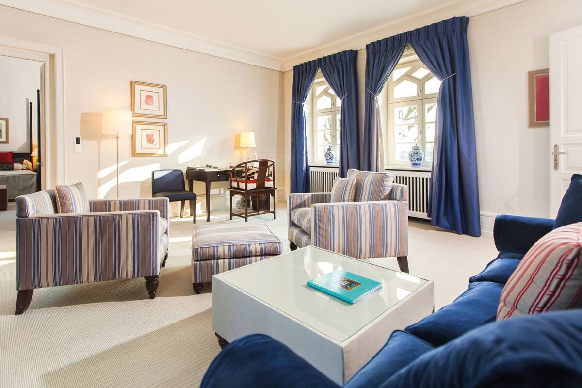 Un salon avec des canapés à rayures, une table basse et une vue sur une chambre à coucher par une fenêtre.