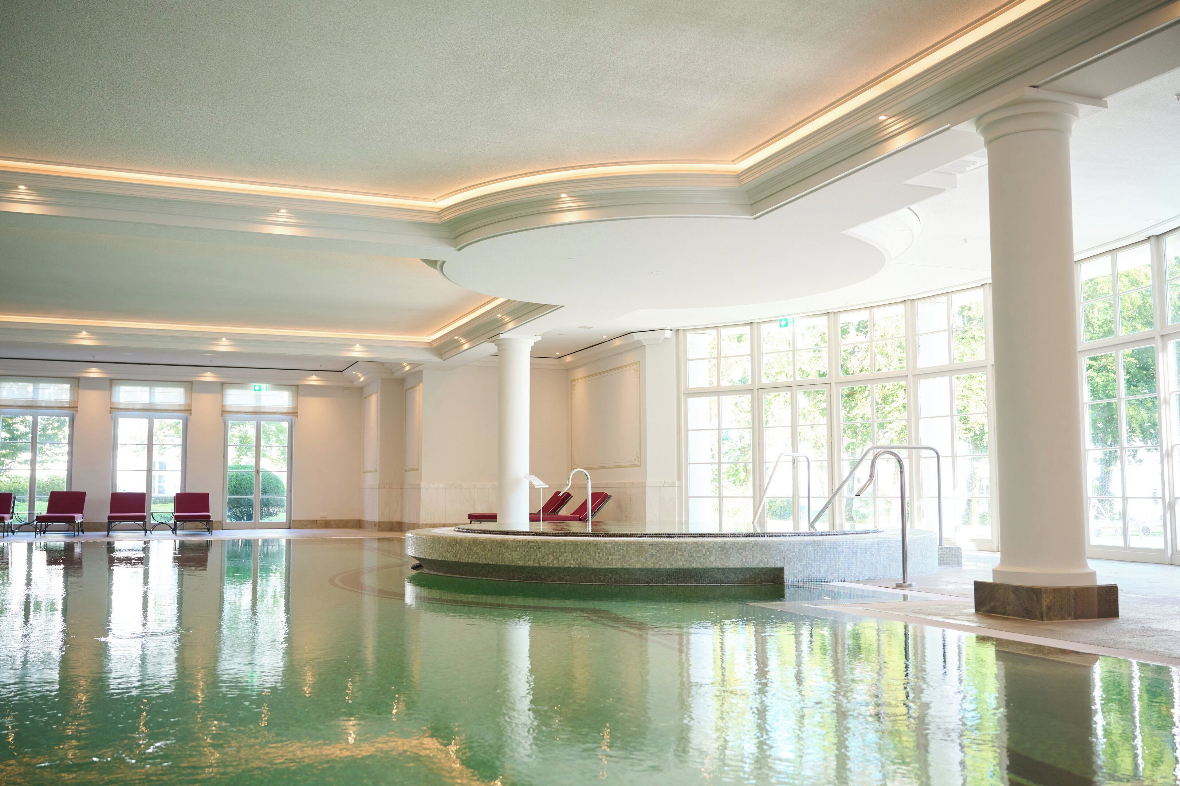 A large indoor swimming pool with a central island, seating areas, and large windows.
