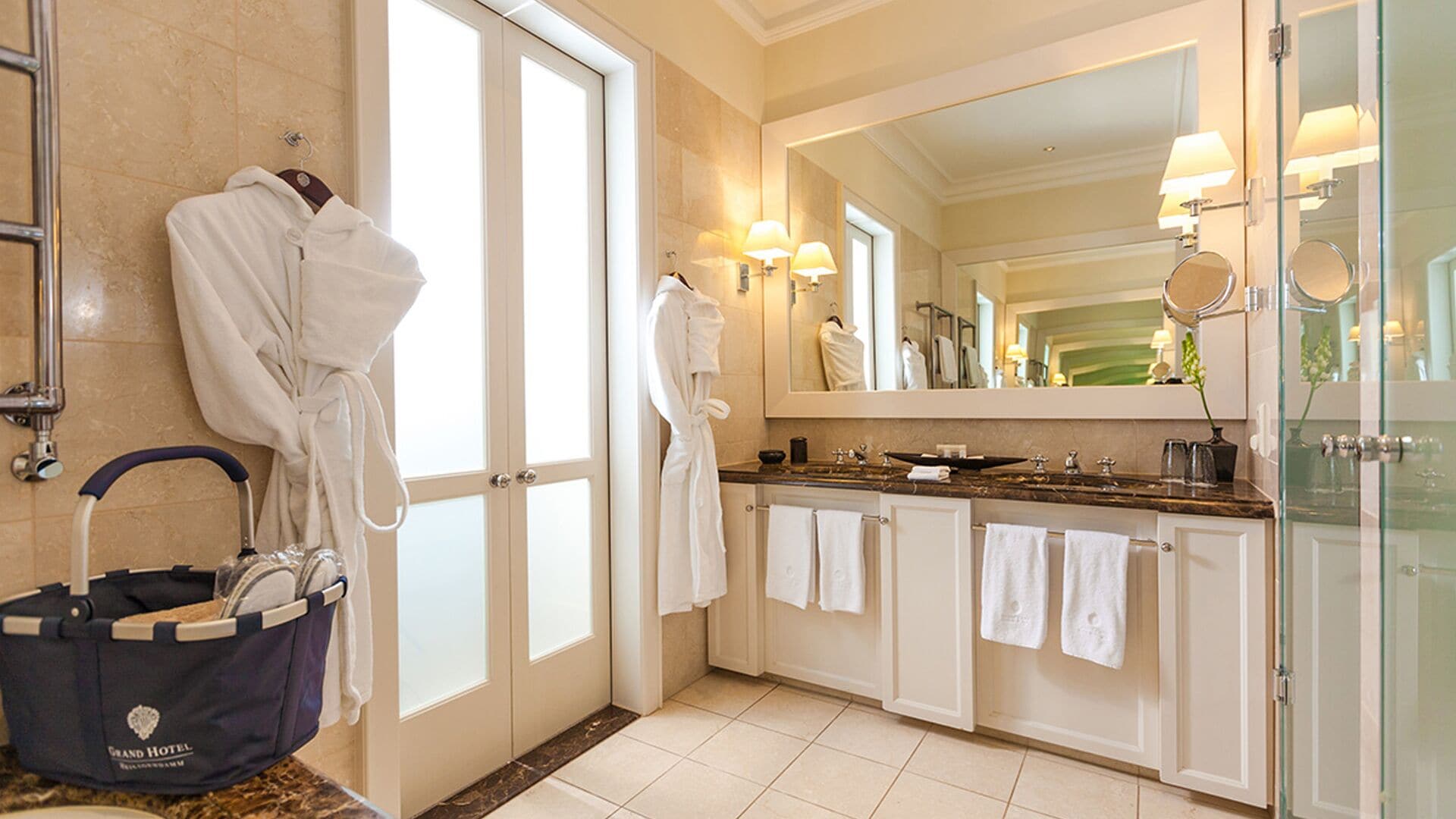 A spacious bathroom with a large mirror, two white towels, a robe, and a bathrobe hanging on a rack.