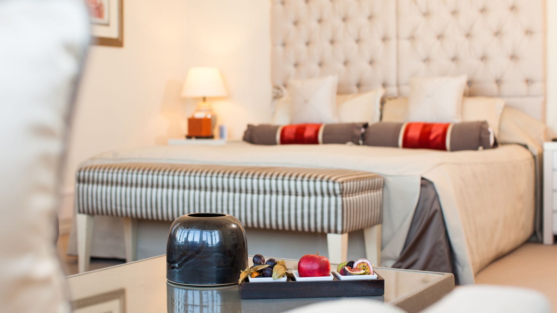 Une chambre à coucher bien rangée, avec un lit, une table de chevet, une lampe et une petite table sur laquelle se trouvent des fruits.