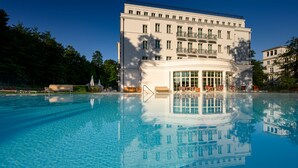 A large building with a pool in front, surrounded by trees and with a clear sky. - Grand Hotel Heiligendamm (Bad Doberan)