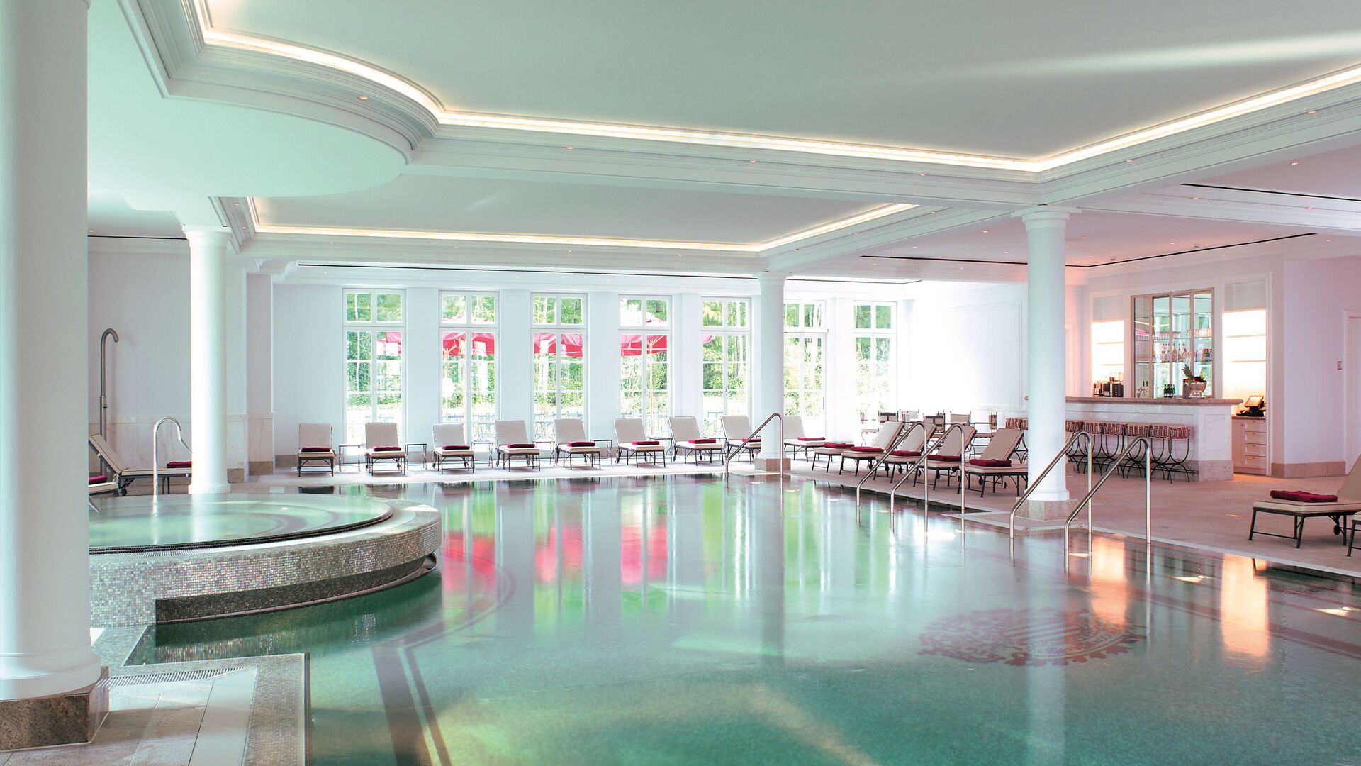 A spacious indoor swimming pool with clear glass walls, allowing natural light to enter.