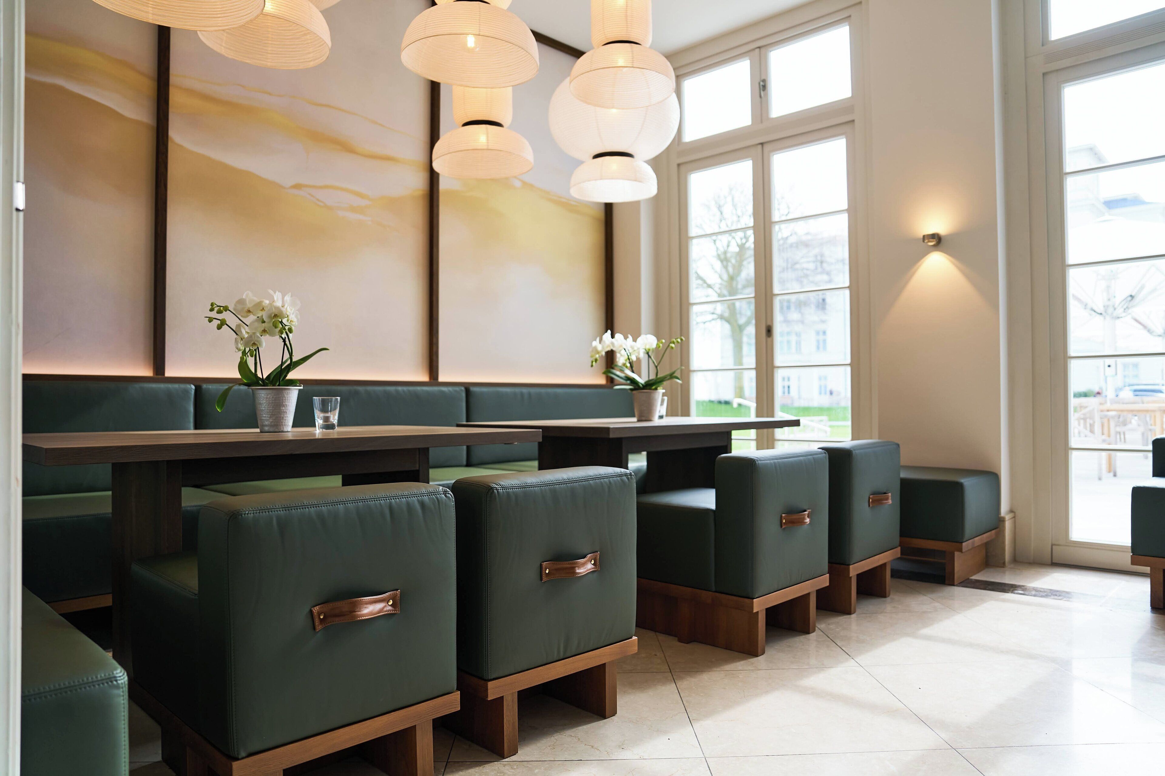 Un interior de restaurante moderno con asientos tapizados en verde, una mesa comunal alargada e iluminación colgante.